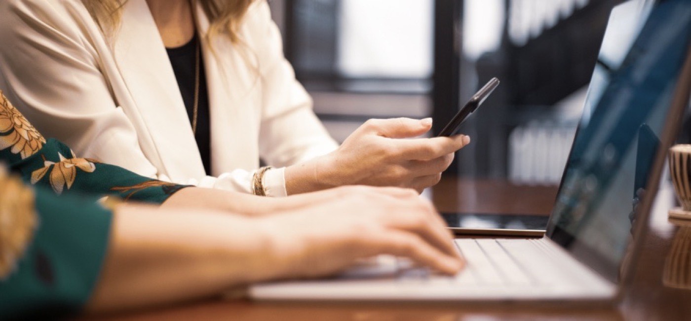 An agent at a desk, phone in one hand, laptop open beside it